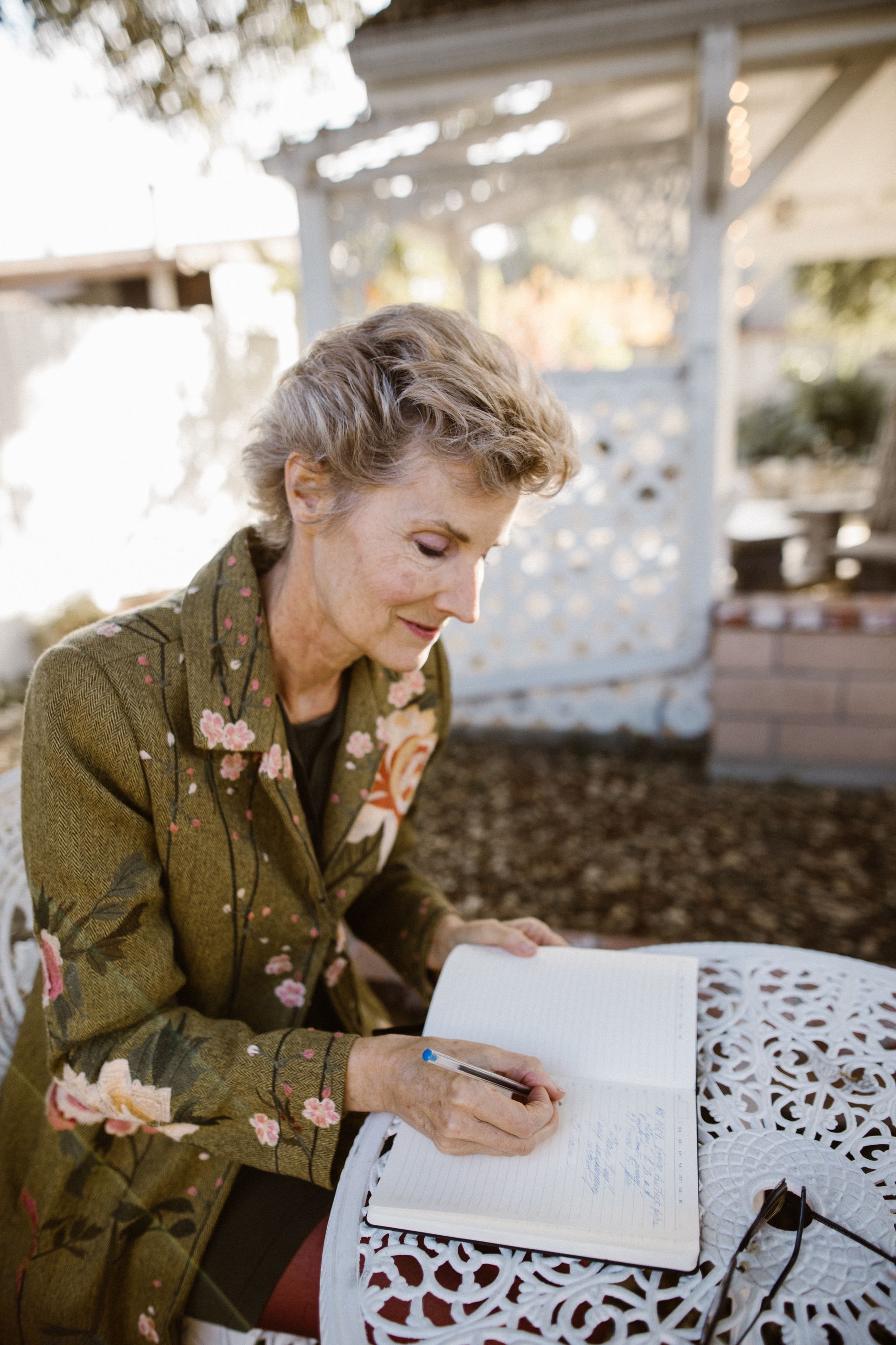 An older woman writing in a notebook outdoors