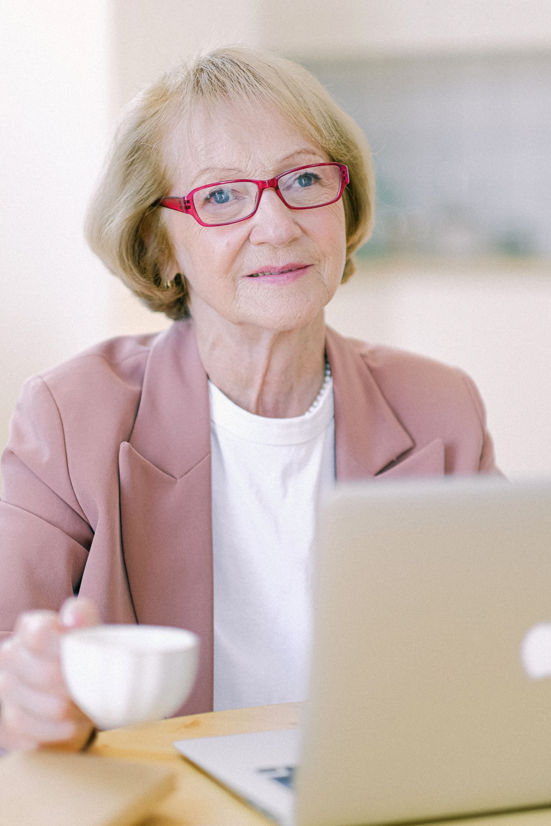 A senior woman working on a laptop at home with a cup of coffee