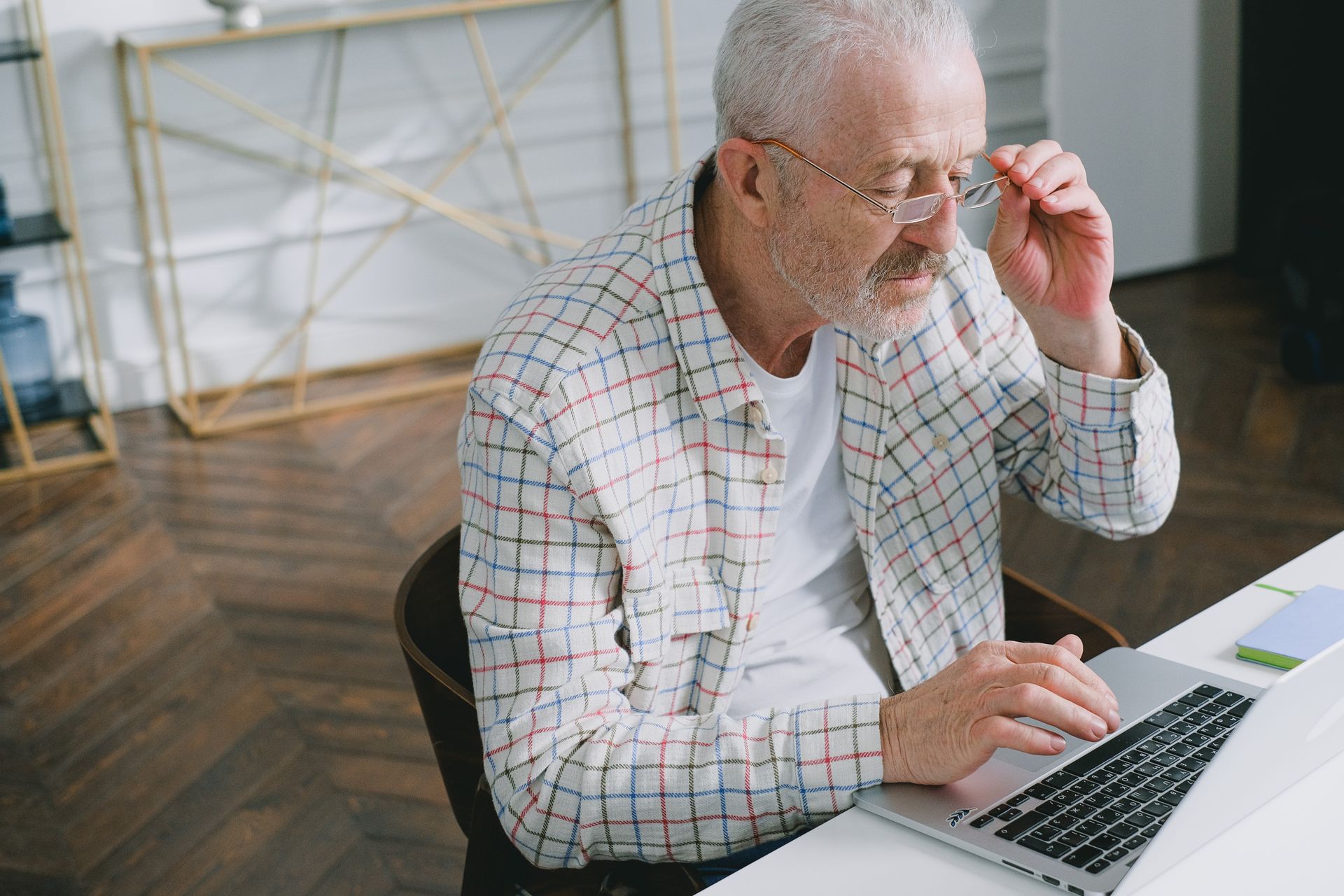 A grey-haired man with glasses thinking at his laptop